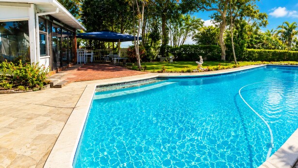 A swimming pool with a curved edge, surrounded by a stone deck and a covered patio area. - Room-tranquil Studio Retreat With Pool a (Westville)