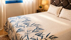Ein Schlafzimmer mit Bett, Vorhängen, Nachttisch, Lampe und einer Wand mit dekorativem Muster.