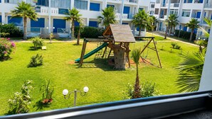 Ein modernes Gebäude mit mehreren Balkonen und einem Spielbereich mit Rutsche und Schaukeln.