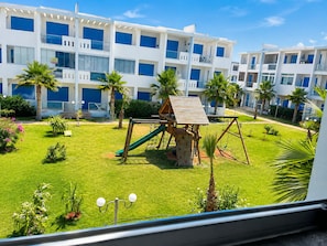 A modern building with multiple balconies and a playground area with a slide and swings. - Pearl Andalusia Seaside Oasis (El Mansouria)