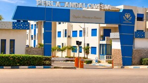 Ein Hotel Eingang mit einer blau-weißen Fassade, einem Schild mit der Aufschrift 'PERLA ANDALOUSSIA' und einem Logo mit einem Diamanten und Flügeln.