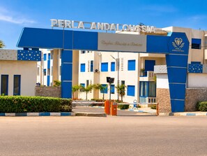 A hotel entrance with a blue and white facade, a sign reading 'PERLA ANDALOUSSIA,' and a logo with a diamond and wings. - Pearl Andalusia Seaside Oasis (El Mansouria)