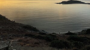 Un paysage côtier avec une mer calme, une petite île et un terrain rocheux à la végétation clairsemée.