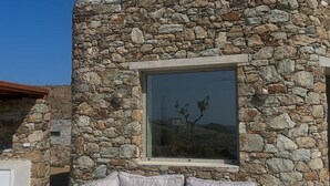Un mur extérieur en pierre, une grande fenêtre, un canapé blanc et une table basse blanche.