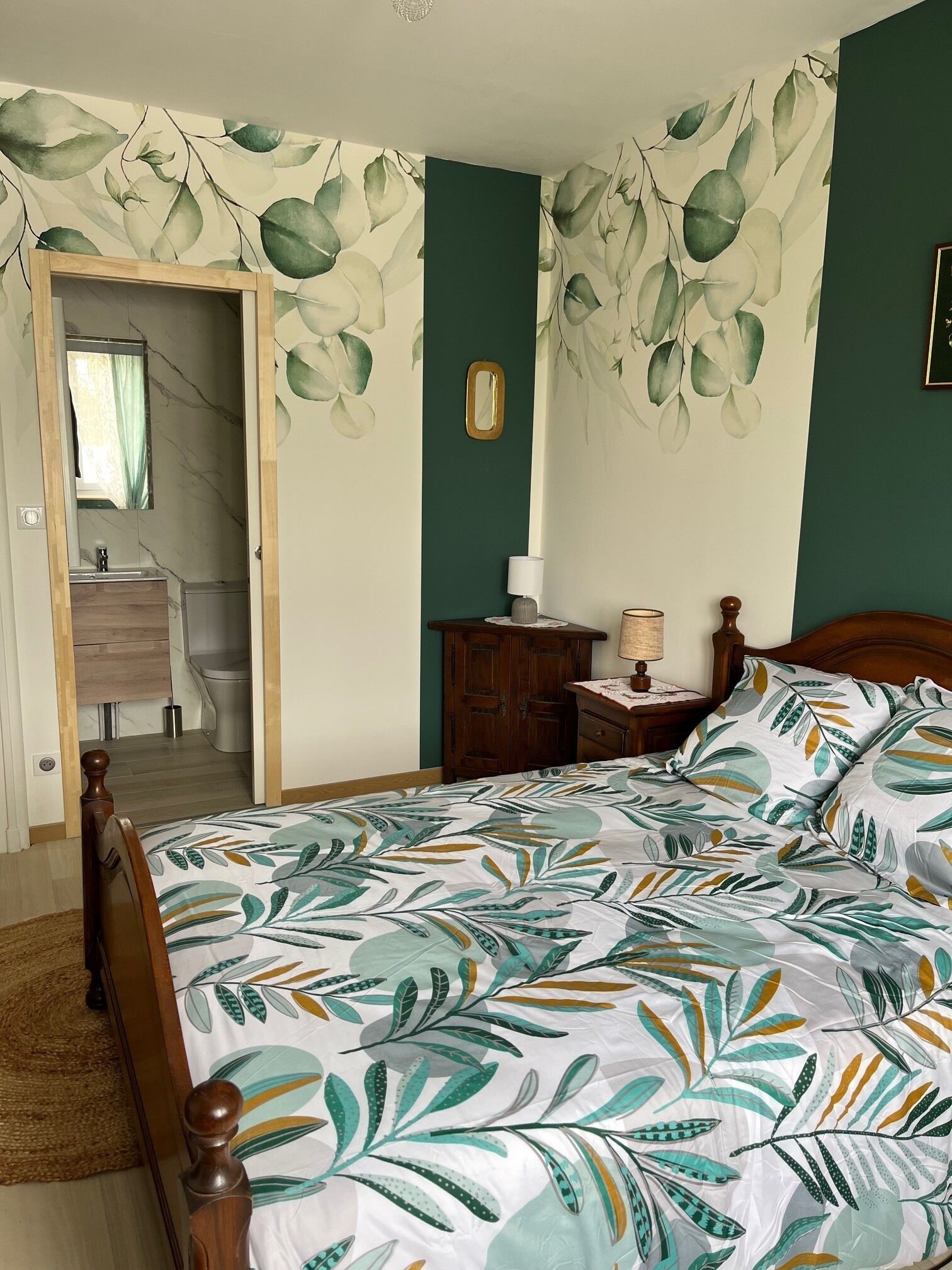 A bedroom with a bed, a nightstand, a dresser, a mirror, and a bathroom visible through an open door.