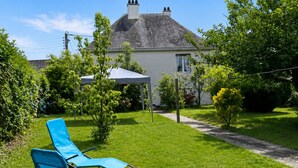 Ein Haus mit Rasen, zwei blaue Liegestühle, einem weißen Sonnenschirm und einem Schornstein.