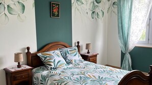 Ein Schlafzimmer mit einem Bett, Nachttischen aus Holz, einer Lampe, einem Deckenventilator und einem Fenster mit Vorhängen.
