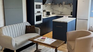 Ein modernes Wohnzimmer mit einer Couch, einem Sessel, einem Couchtisch und einer Küche im Hintergrund.