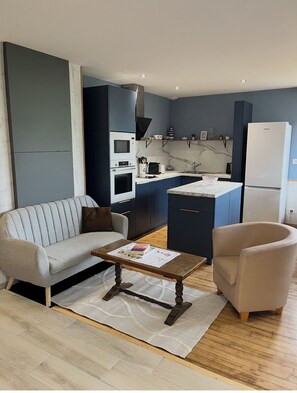 A modern living room with a sofa, armchair, coffee table, and a kitchen in the background. - Pont-Aven vacation home, ideal for families. Pets welcome! (Pont-Aven)