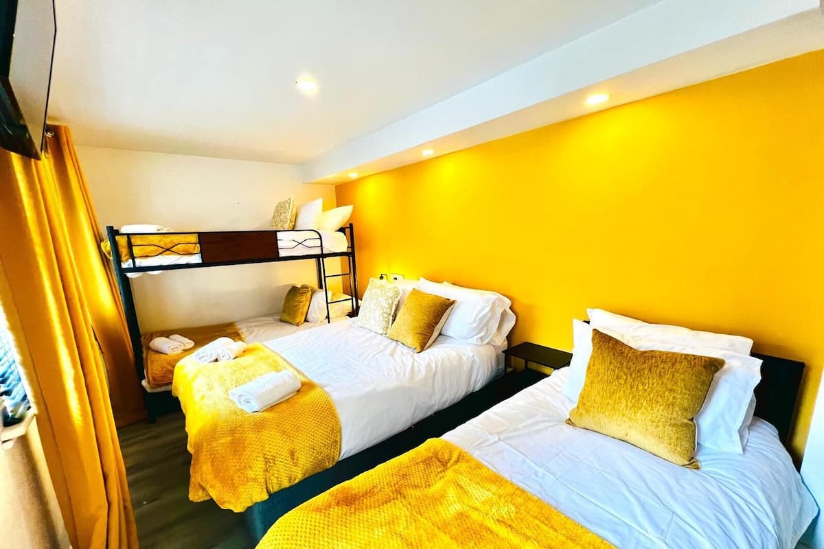 A hotel room with two beds, a bunk bed, yellow walls, and a curtain.