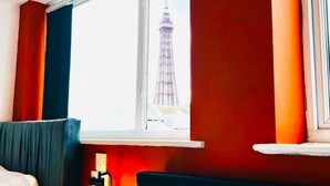 Ein Hotelzimmer mit Bett, einem Fenster mit Blick auf einen hohen Turm und einer Flasche auf dem Nachttisch.