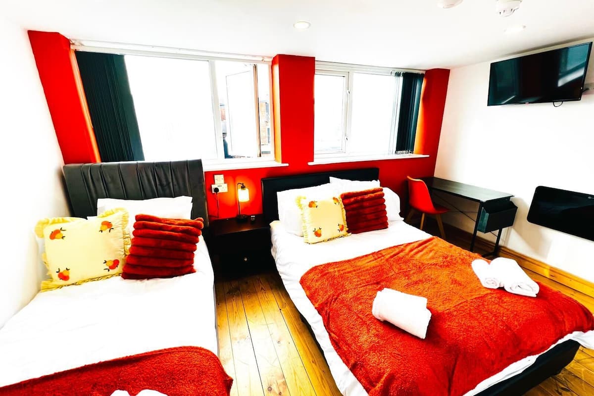 A hotel room with two beds, a desk, a chair, a TV, and a window.