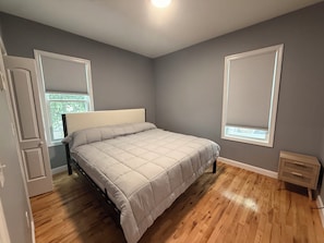 Ein Schlafzimmer mit einem Bett, Holzboden, einer Tür und einem Fenster mit Jalousien.