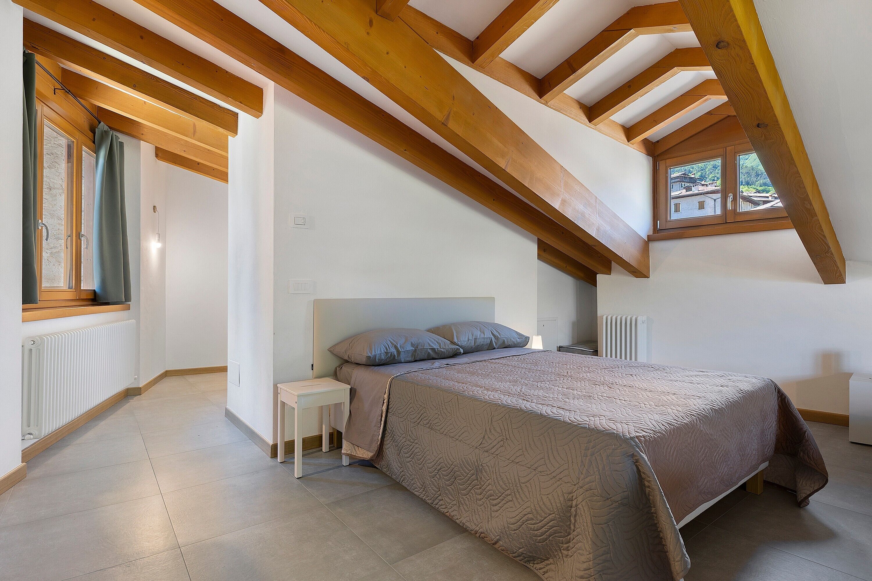 Una camera da letto con soffitto spiovente, un letto, un comodino, una finestra e un termosifone.
