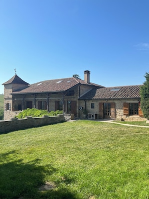 A stone house with a tiled roof, a stone tower, and a grassy yard. - Stone family home with swimming pool (Jalogny)
