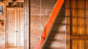 Un intérieur en bois avec un plafond incliné, une porte en bois et une échelle en corde.