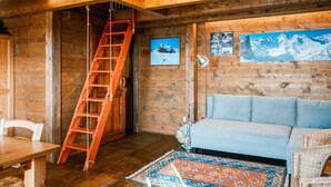 Un intérieur en bois avec un canapé, un tapis à motifs, une échelle et des tableaux encadrés accrochés au mur.