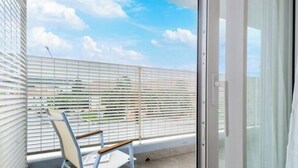 Un balcon avec une chaise, une porte vitrée et une vue sur le ciel et les bâtiments.