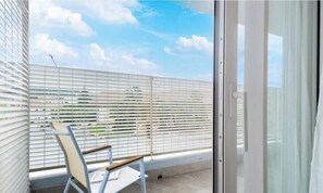 Un balcon avec une chaise, une porte vitrée et une vue sur le ciel et les nuages.