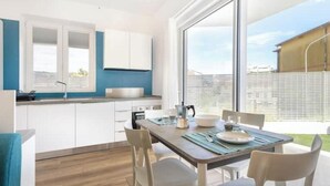Une cuisine moderne avec des meubles blancs, une table à manger en bois et une grande fenêtre.