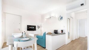 Une cuisine moderne dotée d’un îlot central, d’un coin repas avec des chaises blanches et d’un téléviseur à écran plat fixé au mur.