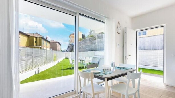 Une cuisine moderne dotée d’un grand îlot central, d’un coin repas avec une table et des chaises, et d’une porte-fenêtre coulissante donnant sur un balcon.