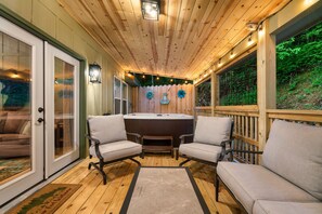 Eine Holzterrasse mit Whirlpool, zwei gepolsterten Stühlen und einer Glastür zu einem Wohnbereich.