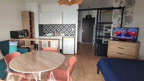Un espace de vie compact comprenant un canapé, une table à manger, des chaises, un coin cuisine et un téléviseur.