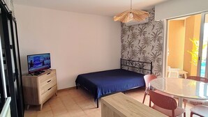 Une chambre à coucher avec un lit, un téléviseur posé sur une commode, un balcon avec des chaises et une table à manger.