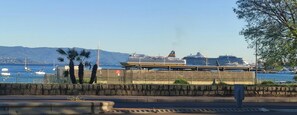 Blick auf das Wasser mit einem vor Anker liegenden Kreuzfahrtschiff, einer Steinmauer und Booten im Hintergrund.