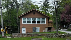 A two-story house with a stone fire pit in the foreground. - Waterfront lake house with private beach and dock with hot  tub on Paradox Lake. (Schroon Lake)