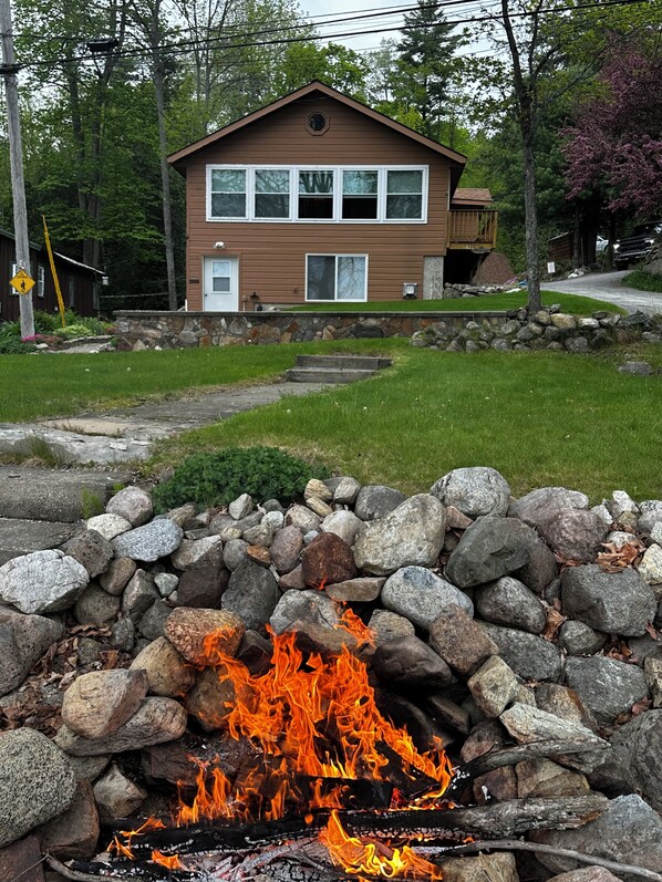 A two-story house with a stone fire pit in the foreground.