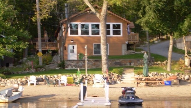 A house with a dock and boats, surrounded by trees and a grassy area. - Waterfront lake house with private beach and dock with hot  tub on Paradox Lake. (Schroon Lake)
