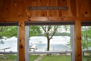 A wooden cabin with a sign reading 'No Charge for the View' and a view of a lake with a dock and boat.