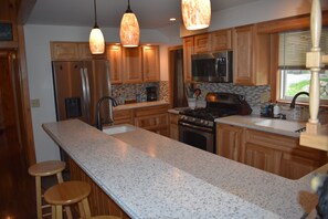 A kitchen with wooden cabinets, a stainless steel refrigerator, a gas stove, and a granite countertop.
