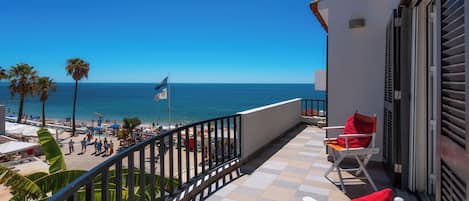 A balcony with a view of the beach and ocean, a flag, and outdoor seating.