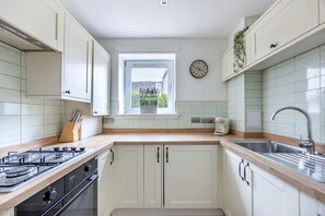 Eine Küche mit weißen Schränken, einem Gasherd, einer Spüle und einem Fenster mit Blick auf Grünflächen.