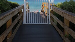 Une promenade en bois menant à une plage, avec une barrière blanche à l’entrée.
