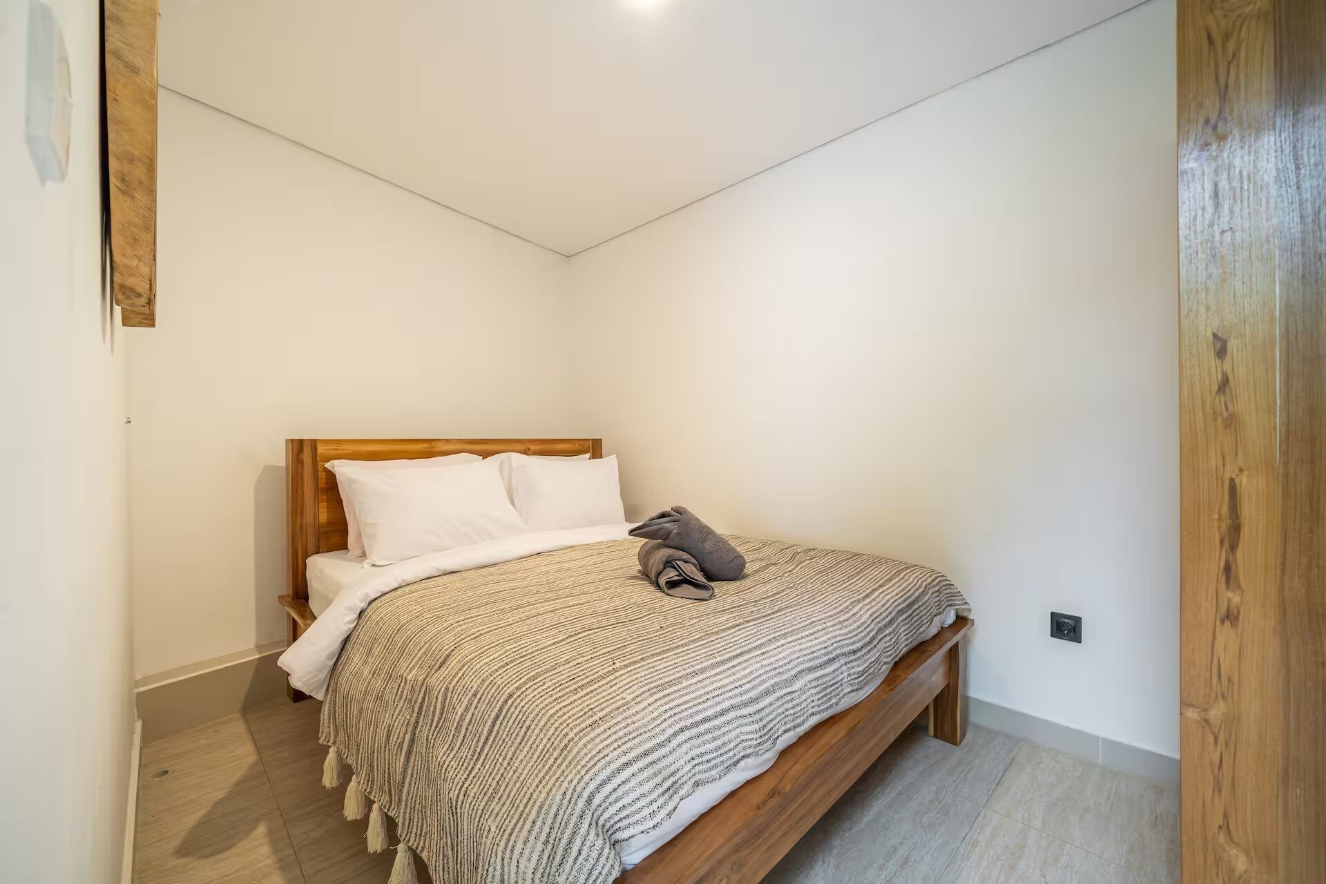 Un dormitorio con cama de madera, almohadas blancas, manta a rayas y una pequeña mesita de noche.