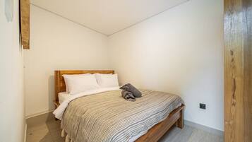 Un dormitorio con cama de madera, almohadas blancas, manta a rayas y una pequeña mesita de noche.