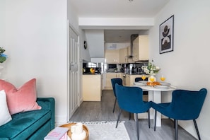 Ein kompakter Wohnbereich mit einem blauen Sofa, einem Essbereich mit blauen Stühlen, einer Küche im Hintergrund und einem gerahmten Bild an der Wand.