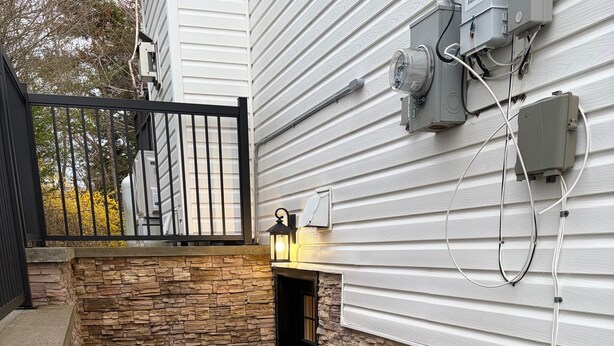 A stone-walled outdoor area with a welcome mat, a metal bench, and a lantern. - Entire Apartment in Bedford (Bedford)