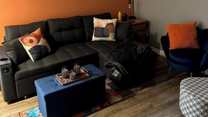 A modern living room with a sectional sofa, a coffee table, a patterned ottoman, a blue armchair, and a colorful abstract painting on the wall. - Entire Apartment in Bedford (Bedford)