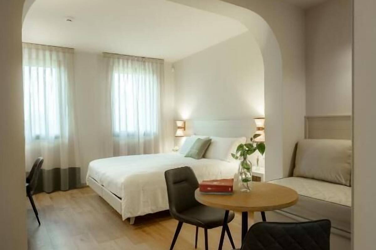 Habitación de hotel con cama, una mesa redonda con sillas, un sofá y una pequeña mesa con un florero.