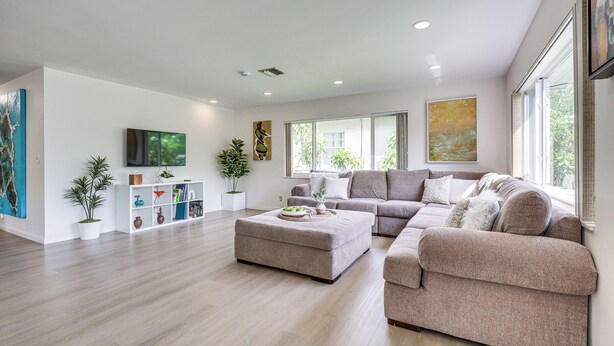 A modern living room with a sectional sofa, ottoman, and a bookshelf. - Beautiful, Calm, Modern Home with a Large Playroom (Hallandale Beach)