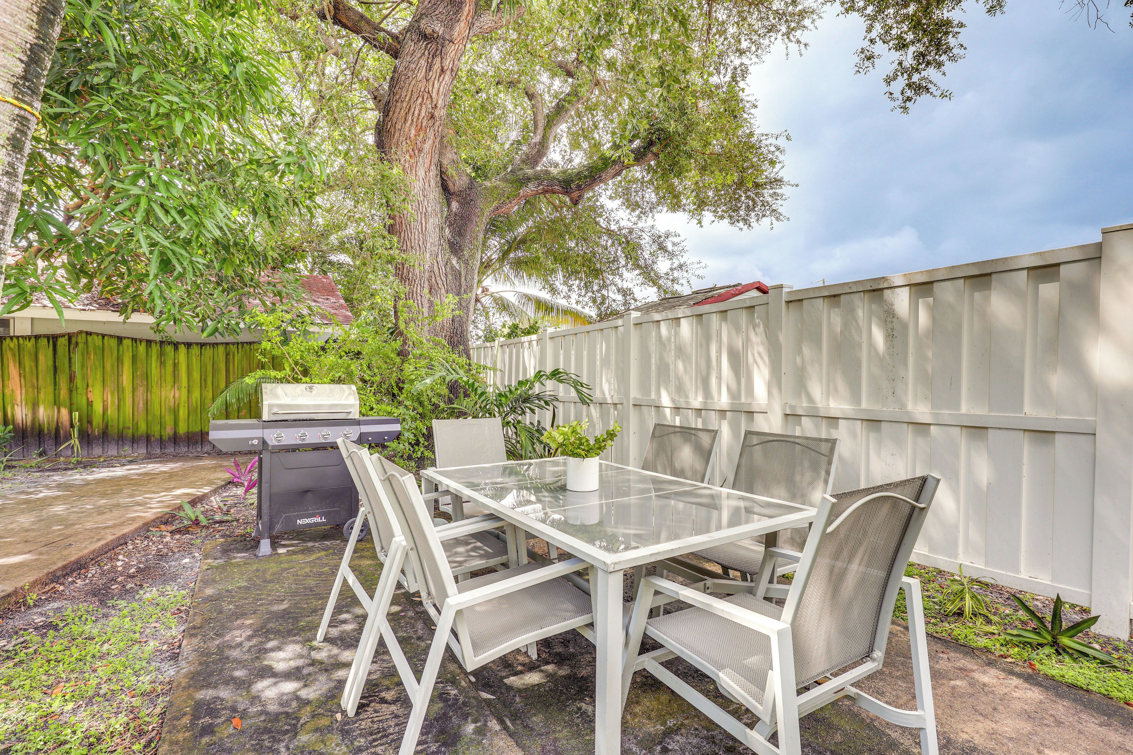 Une terrasse avec une table et des chaises en verre, un barbecue et une clôture blanche.