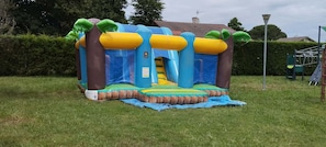 An inflatable play structure in a grassy area with a slide, surrounded by trees and a house in the background. - Mobile home in a 4-star campsite (Aureilhan)