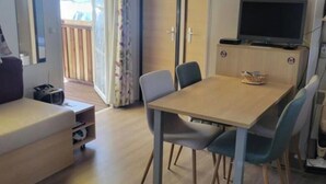 Ett rum med ett matbord och stolar i trä, en soffa, en tv och en luftkonditioneringsanläggning.