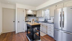 Una cucina con mobili bianchi, un frigorifero in acciaio inossidabile, un tavolo di legno e un forno a microonde.