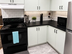 Una cocina con armarios blancos, estufa negra y refrigerador de acero inoxidable.